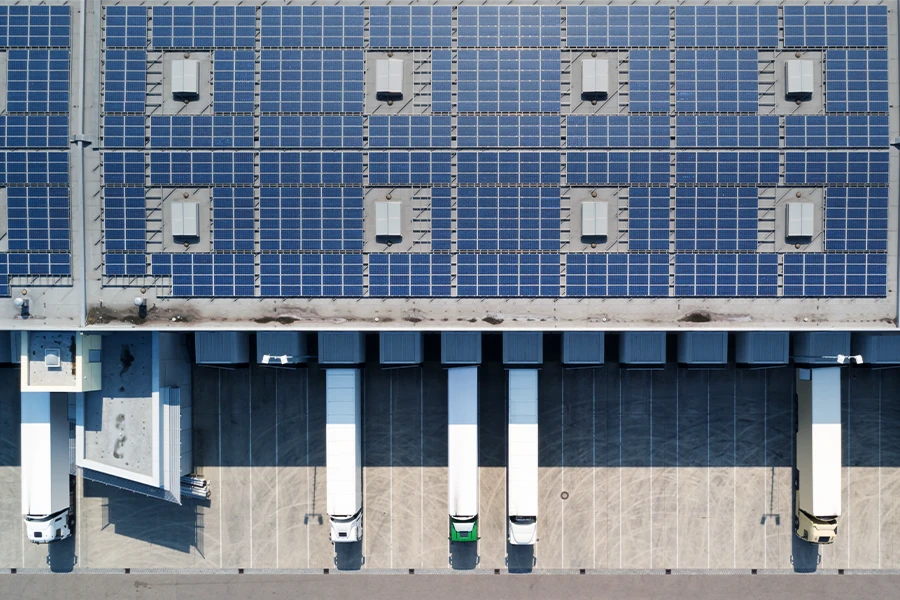 Aerial view of a logistics facility with rooftop solar panels and electric trucks at loading docks