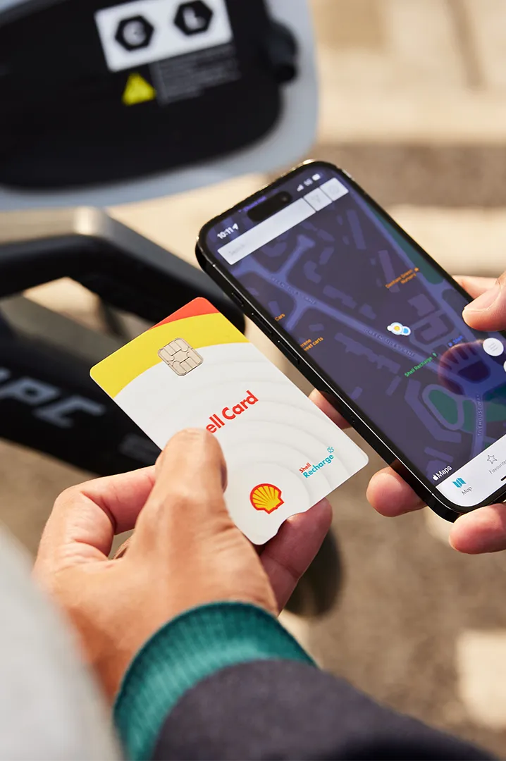 Person holding Shell Card and smartphone showing EV charger locations in the Shell App