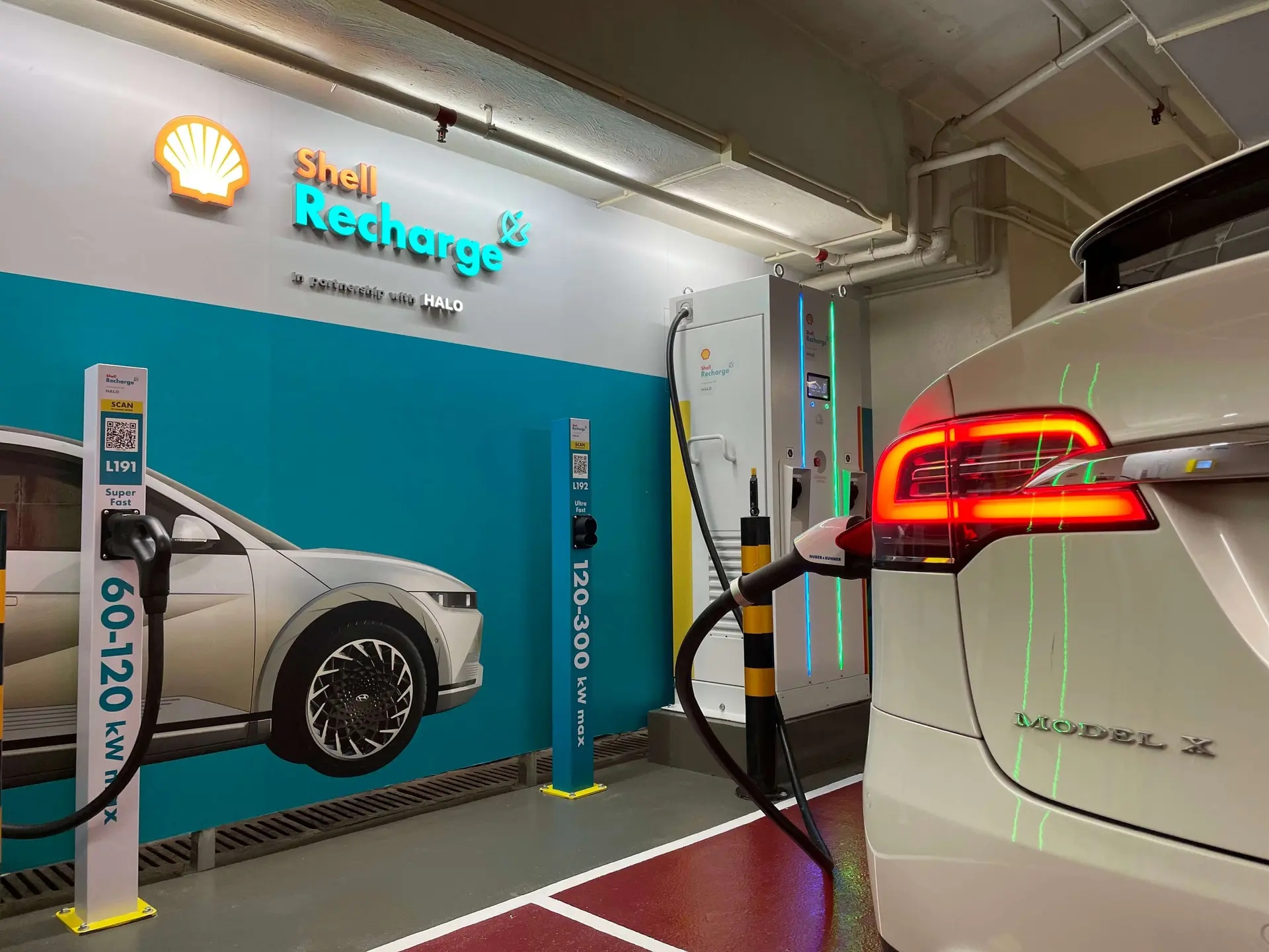 Ladestation für Elektrofahrzeuge mit Shell Recharge- und Halo Energy-Branding, an der ein Elektrofahrzeug in einer Innenanlage mit einem Schnellladegerät verbunden ist.